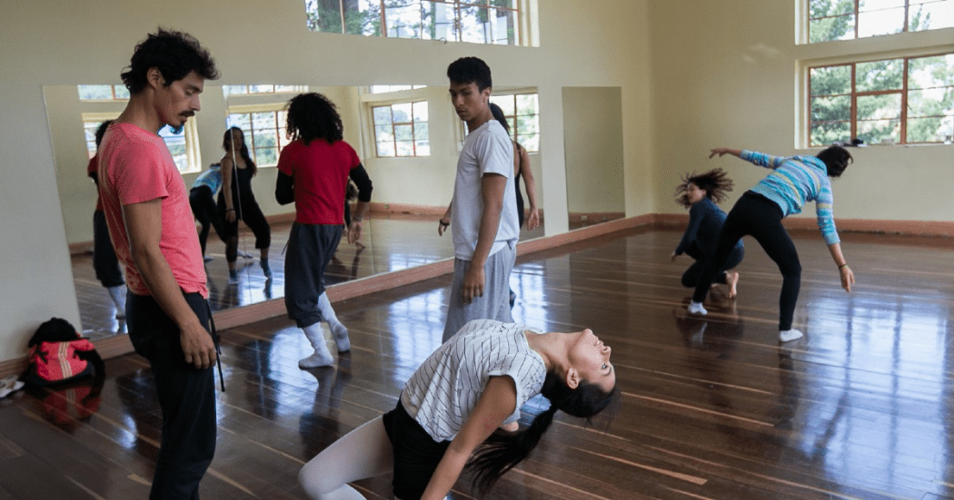 Imagen de una bailarina de rodillas en posición de pilates y al lado se encuentra su instructor