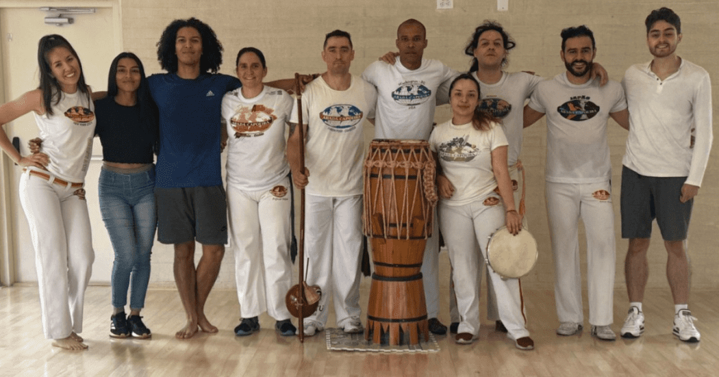 Imagen de varios participantes de una clase de capoeira de los cuales uno de ellos porta un tambor 