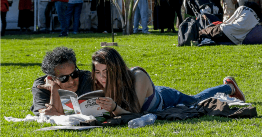 Imagen de un hombre y una mujer acostados en el pasto de un parque leyendo un libro.