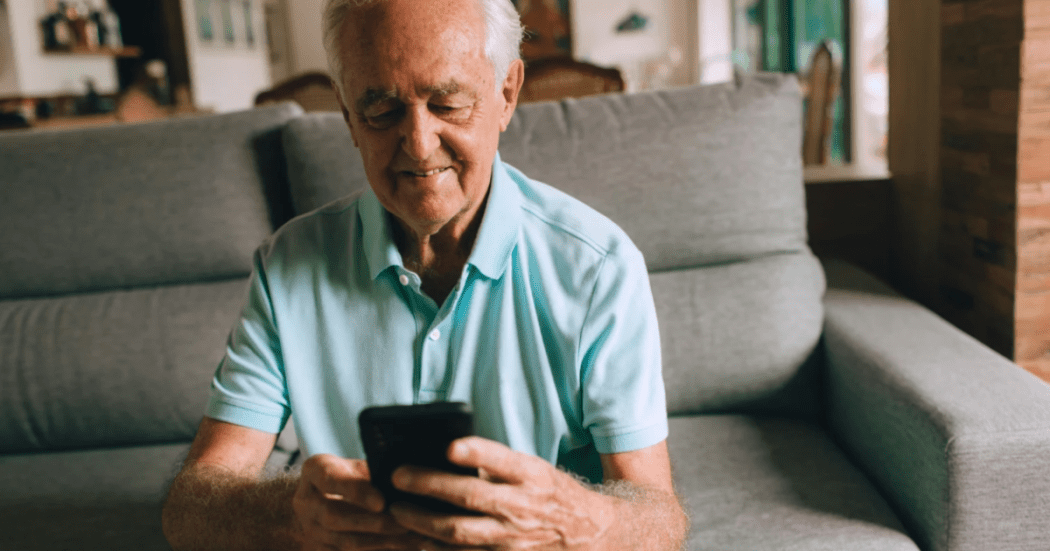 Imagen de un hombre adulto mayor sentado mirando su celular.