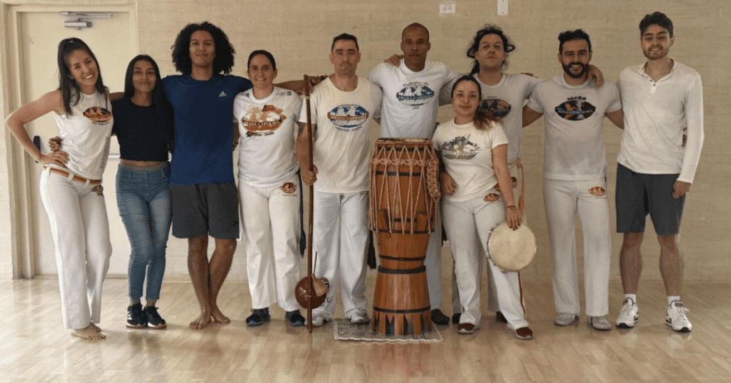 Imagen de varios participantes de una clase de capoeira de los cuales uno de ellos porta un tambor 