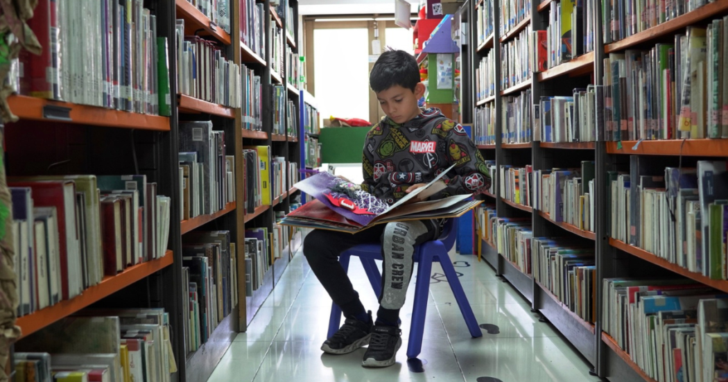 Imagen de un niño leyendo un libro en medio de un stand de libros en las Bibliotecas públicas de Bogotá