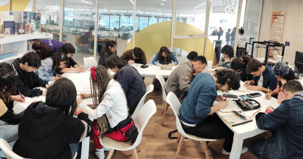 Imagen que muestra varias personas reunidas en un salón escribiendo en un papel 