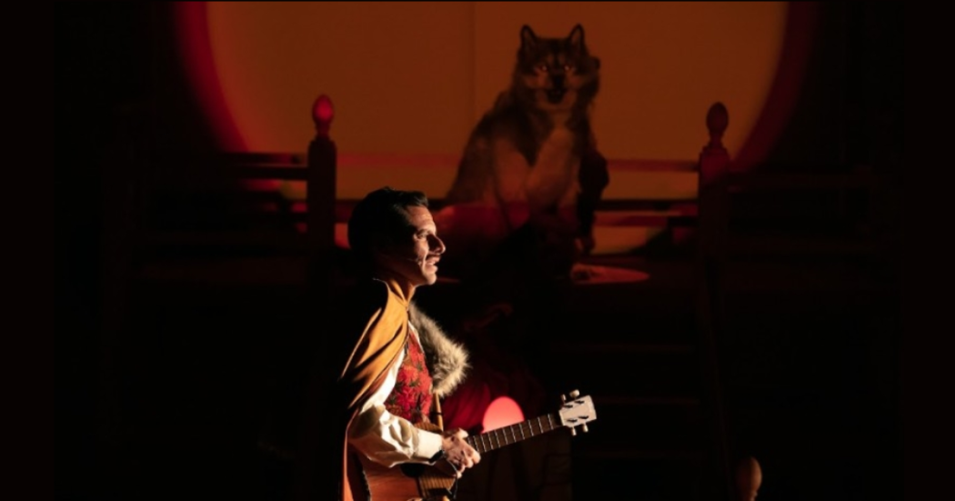 Imagen de un bombre que toca guitarra y al fondo se ve un lobo.