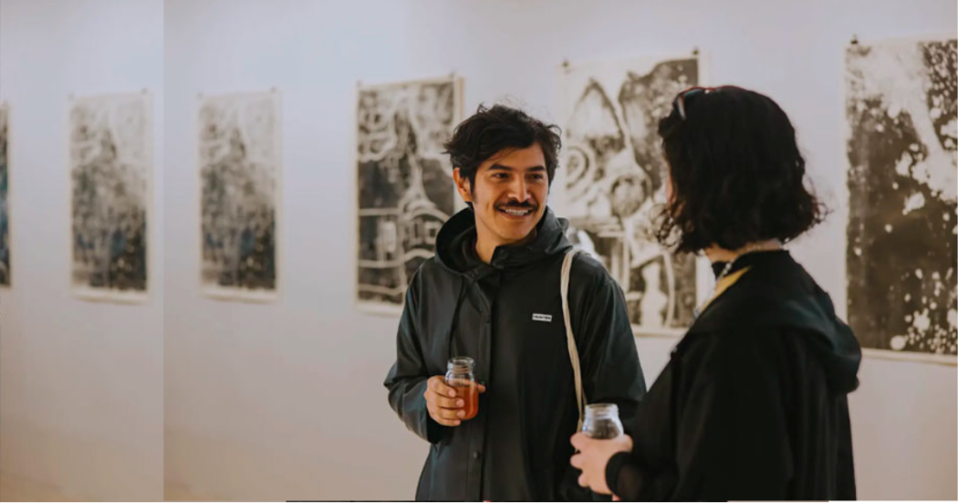 Imagen de un hombre y una mujer en un recorrido por la exposición, al fondo se ven cuadros expuestos.