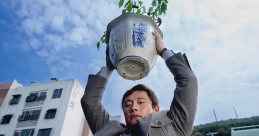 Imagen de un hombre que levanta en sus manos una matera blanca en la que hay una planta verde.