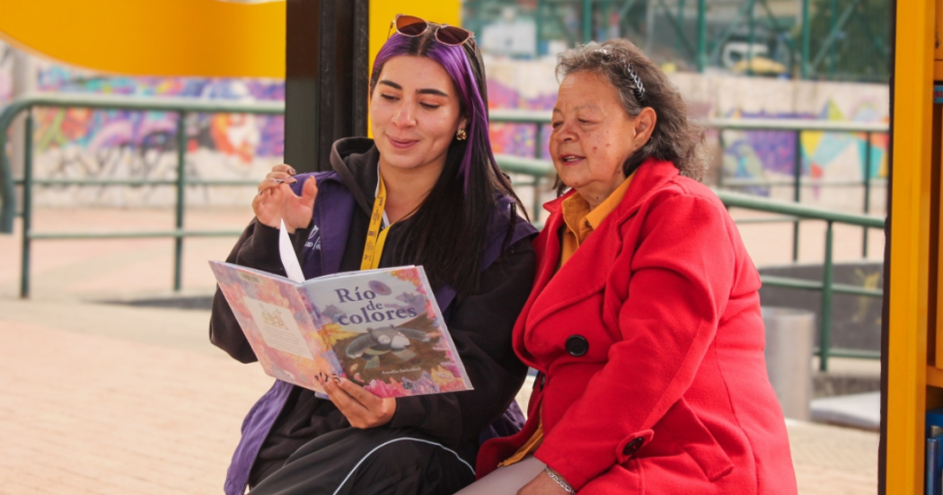 Imagen de una funcionaria de BibloRed leyendo un libro con una usuaria en un Paraderos Paralibros Paraparques de BibloRed