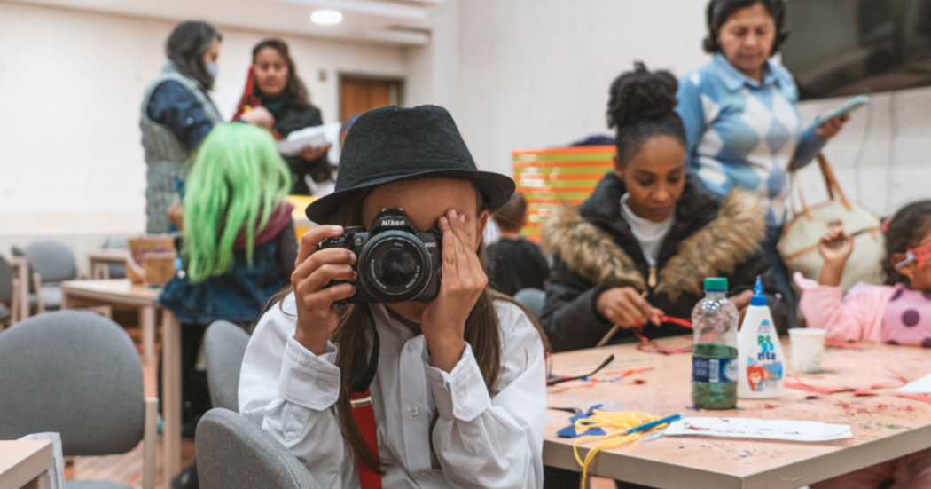 Imagen de niño con una cámara fotografica con personas de fondo en tallerres de manualidades de BibloRed