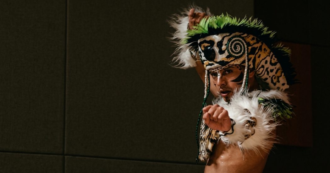 Imagen de un hombre indigena que lleva gorro de plumas en su cabeza.