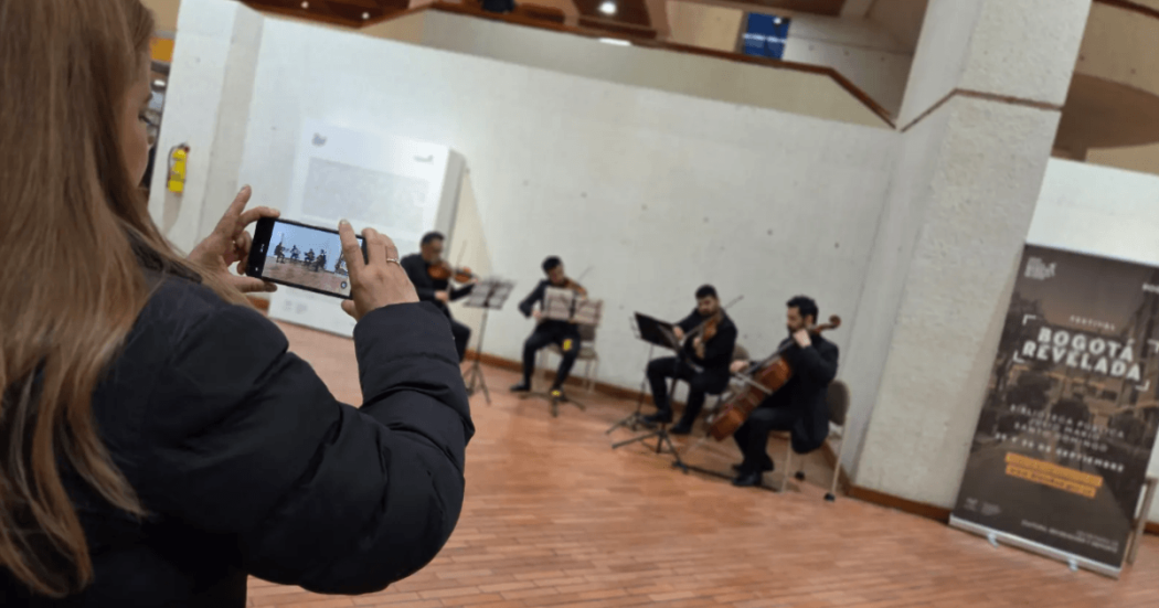 Imagen de una mujer tomando una fotografía con el celular a grupo tocando violines