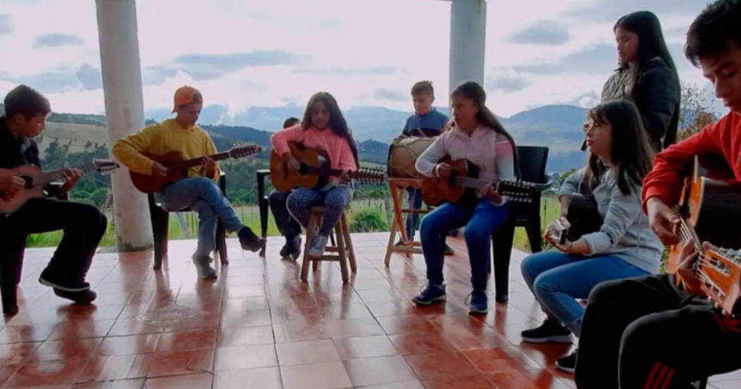 Imagen de varios jóvenes sentados tocando guitarra, de fondo se ve la naturaleza.