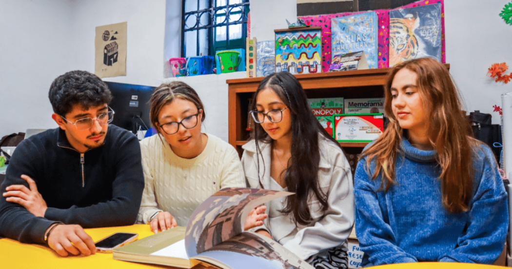 Imagen de 3 mujeres y un hombre mirando un libro abierto en las bibliotecas públicas de Bogotá
