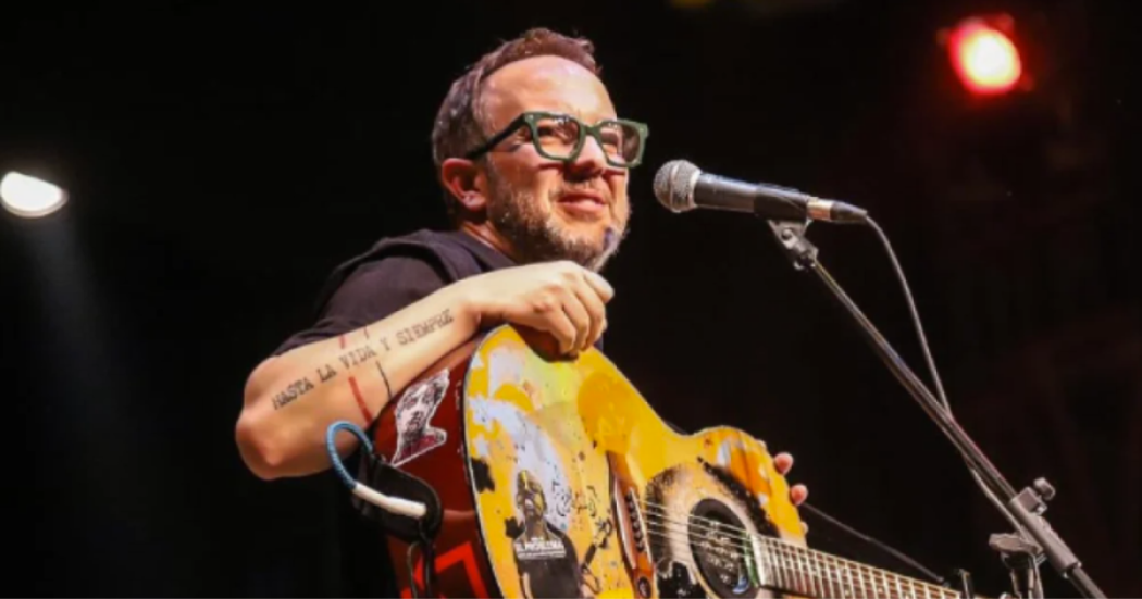 Imagen del cantante César López en un escenario donde lleva una guitarra en sus manos.