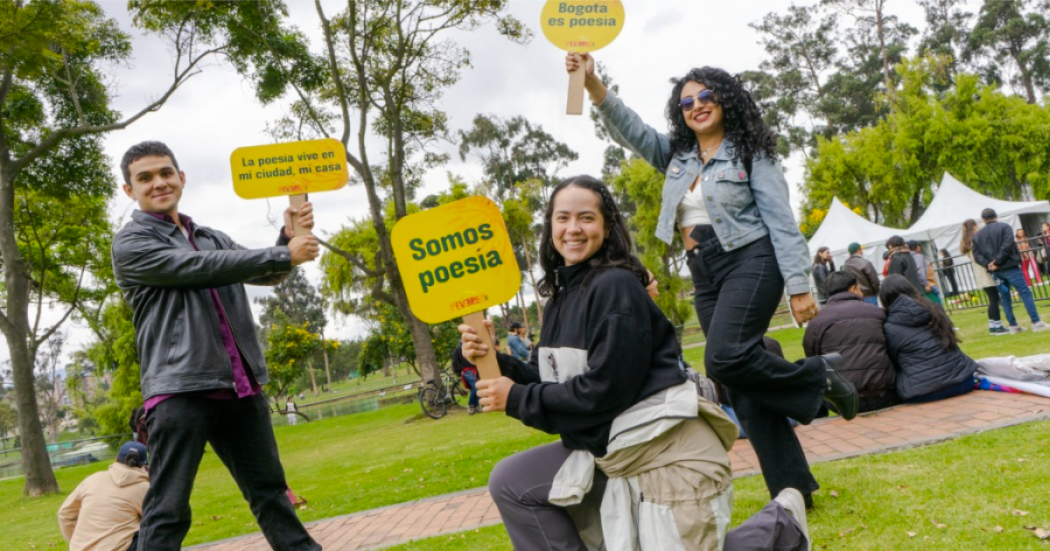 Imagen de dos mujeres jóvenes y un hombre que se encuentran en un parque, en sus manos llevan carteles con info del Festival Reverso.