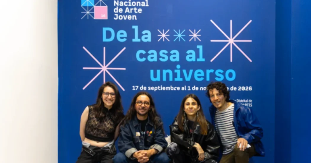 Imagen de dos hombres y dos mujeres que son los expositores de ´De la casa al universo` atras de ellos se ve el cartel promocional de la exposición.