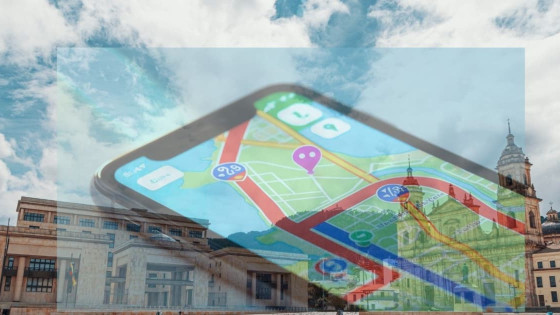 Foto de la Plaza de Bolívar en la que sobresalen el Palacio de Justicia y la Catedral Primada recubiertas por una silueta de un teléfono movil con un mapa. El cielo es de color azul con nubes blancas.