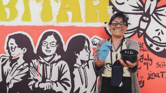 Mujer sonriente frente a un mural que ayudó a pintar.