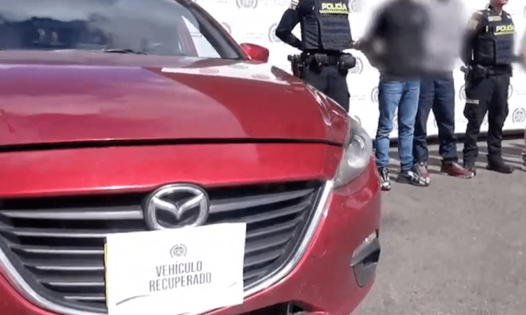 Imagen de un vehículo rojo y al lado hombres y agente de Policía de pie.