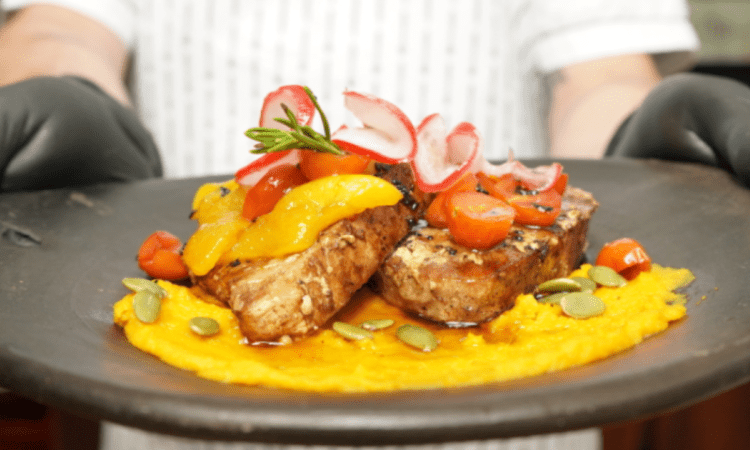 Imagen de una persona que tiene en sus manos un plato de una carne emplatada de manera típica.