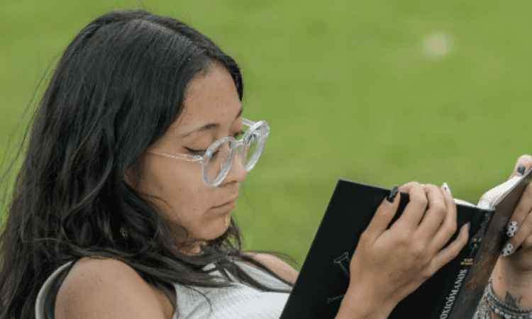 Imagen de una mujer leyendo un libro, sentada comodamente en un parque.