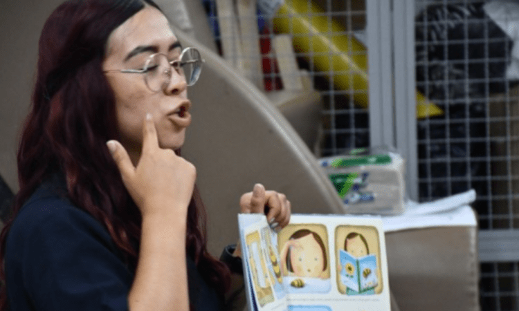 Imagen de una profesora con un libro en el que se ve una ilustración