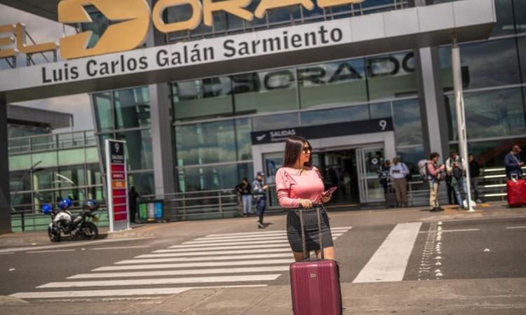 Foto de una mujer con su maleta de viaje frente al Aeropuerto Internacional El Dorado de Bogotá.