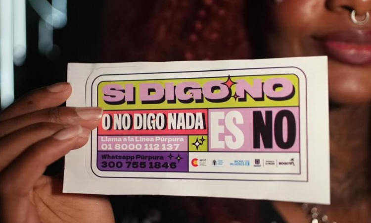 Mano de mujer sosteniendo un volante que dice: "Si digo no o no digo nada, es no. Llama a la Línea Púrpura".