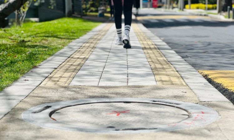 Foto que muestra una persona caminando por un andén en el que se ve una tapa de alcantarillado