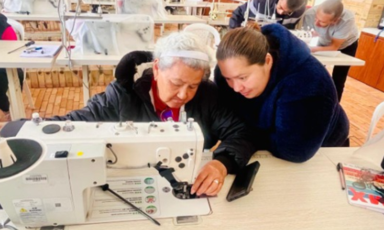 Imagen de una adulta mayor acompañada de una señora cosiendo