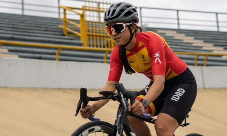 Paradeportista del Equipo Bogotá entrena ciclismo de pista en velódromo, usando casco y uniforme institucional rojo y amarillo, mientras pedalea sobre superficie inclinada con graderías metálicas al fondo.
