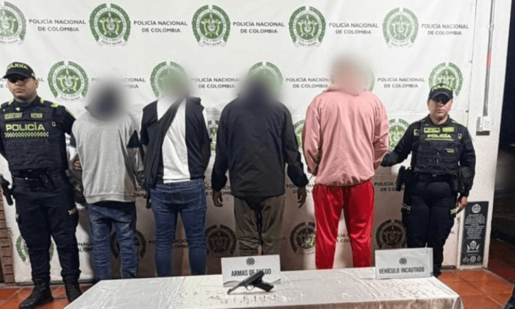 Cuatro capturados en medio de dos policías. El arma incautada está sobre una mesa.