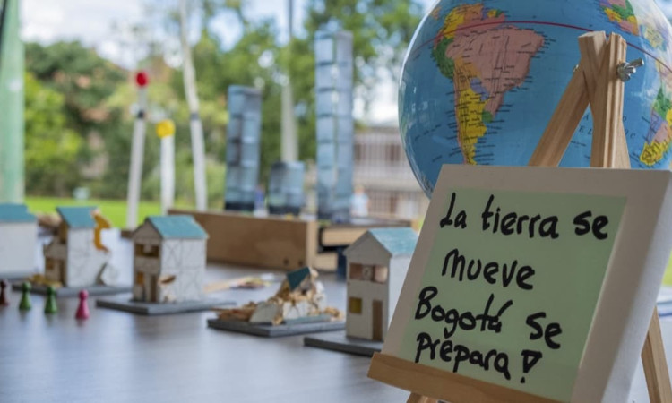Mesa educativa sobre sismos con maquetas, globo terráqueo y cartel con texto “La tierra se mueve Bogotá se prepara!”.