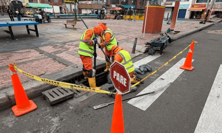 Foto que muestra dos personas con uniforme de Aguas Bogotá limpiando un sumidero