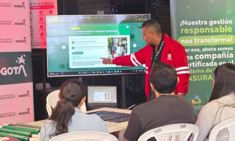 Foto que muestra personas sentadas y un señor señalando un televisor 