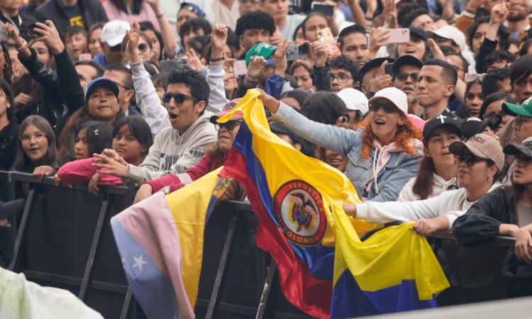 Asistentes a concierto en el parque Simón Bolívar permanecen frente a valla de seguridad del escenario, con banderas de Colombia visibles en primer plano.
