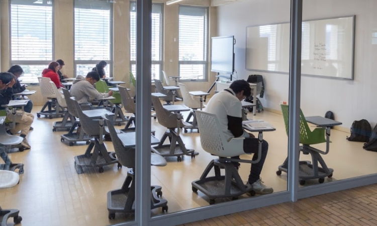 Foto que muestra estudiantes sentados en escritorios dentro de un salón 