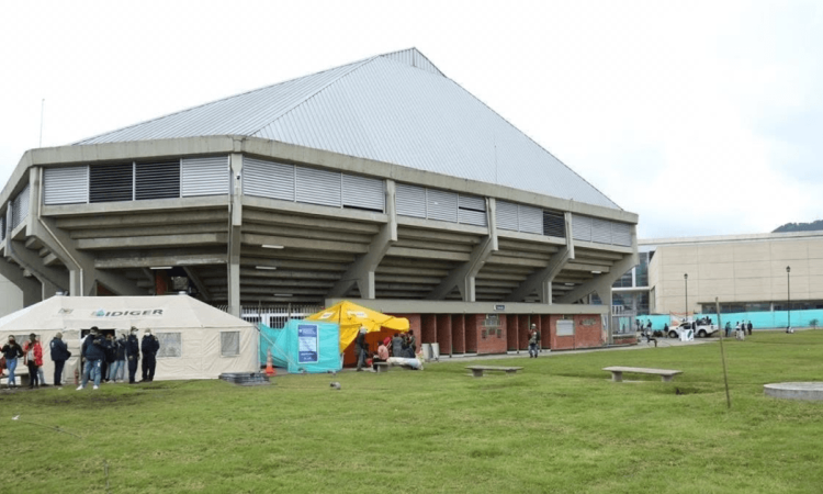 Vista exterior del Palacio de los Deportes en Bogotá con carpas institucionales, personas y un punto de recepción de ayudas humanitarias instalado sobre una zona verde.