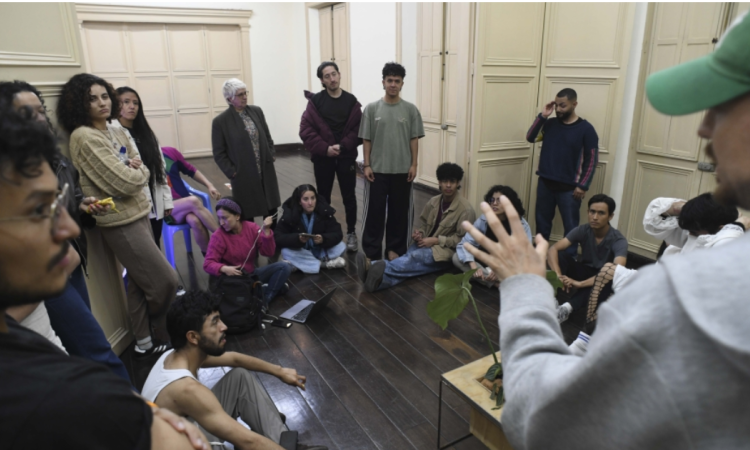 Imagen de varios jóvenes en una aula escuchando a un hombre mayor que habla.