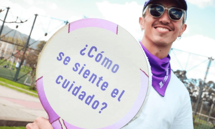Hombre sosteniendo una pancarta que dice "¿Cómo se siente el cuidado?".