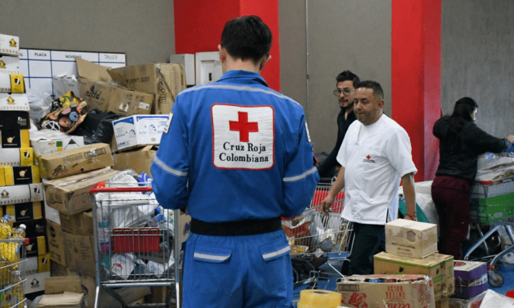 Personal de la Cruz Roja Colombiana organiza y clasifica donaciones en un centro de acopio con cajas, mercados, elementos de ayuda humanitaria y carritos de transporte en Bogotá.