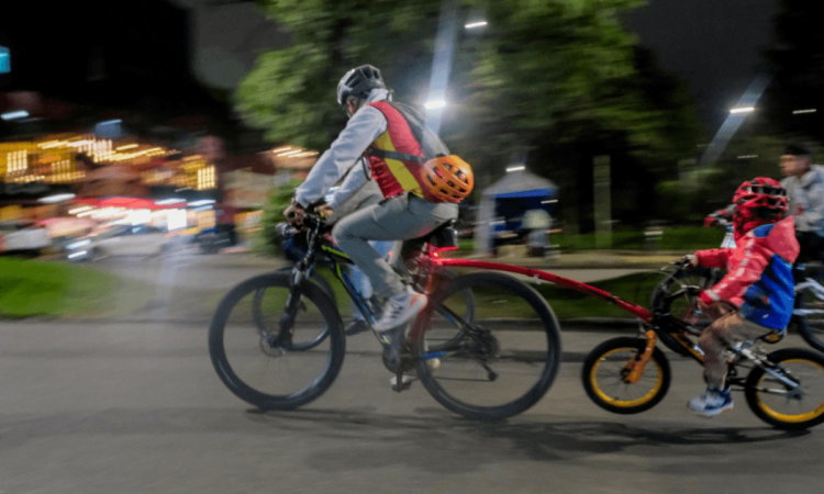 Persona adulta y menor de edad recorren una vía en bicicleta durante una jornada nocturna en Bogotá.