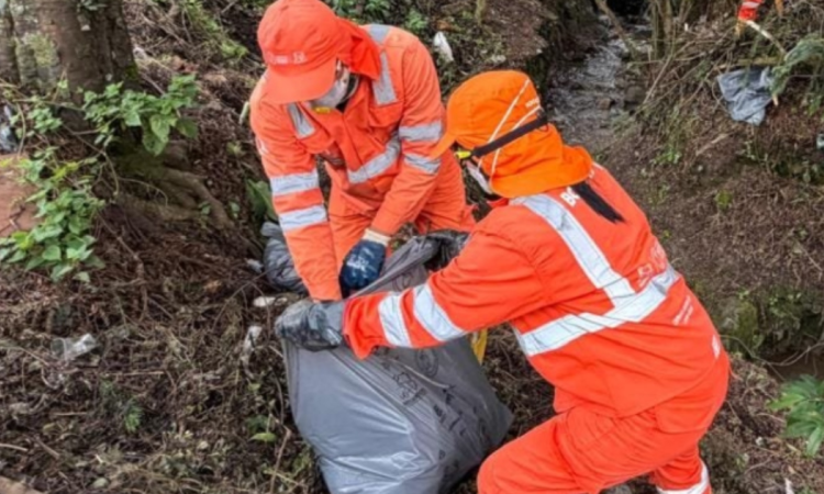 Foto que muestra dos personas levantando una bolsa con residuos 