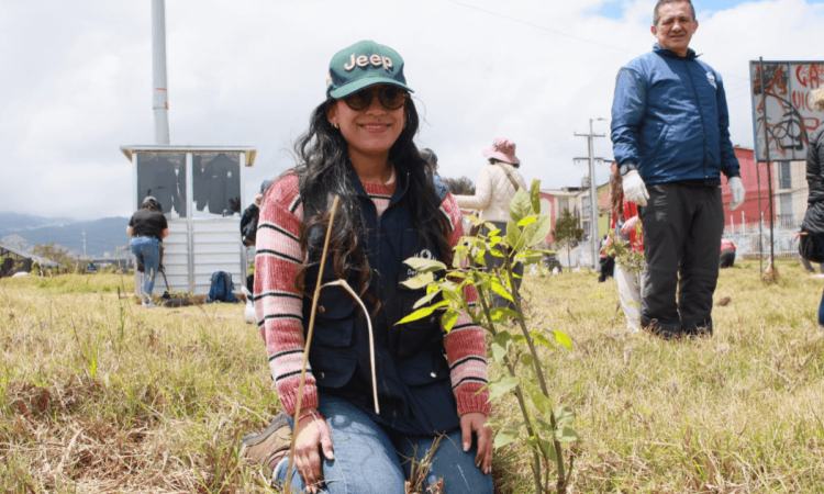 Persona participante de una actividad ambiental sostiene una plántula junto a vegetación nativa en un humedal de Bogotá, durante una jornada de formación y conservación ambiental.