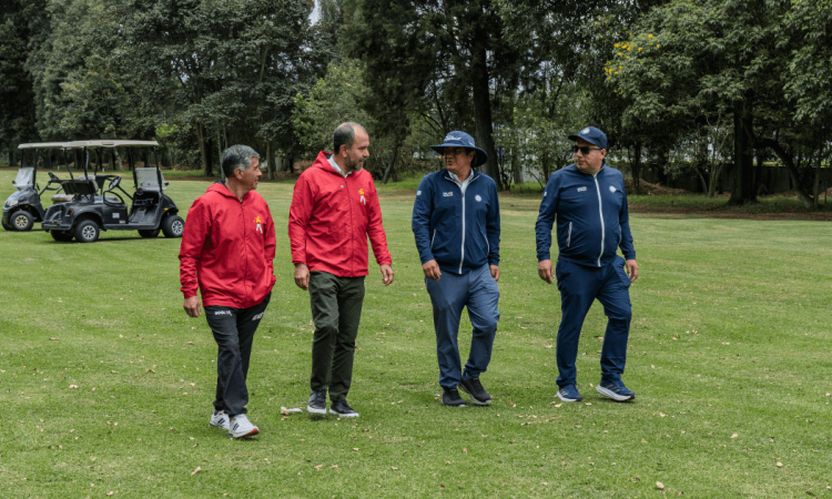 Cuatro personas caminan sobre el césped del campo de golf del Parque La Florida. Dos visten chaquetas rojas y dos chaquetas azules.
