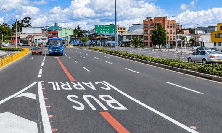 Carril preferencial para buses en la calle 63 de Bogotá, con un bus azul circulando por la vía, señalización vial pintada sobre el pavimento, separadores con vegetación y edificios al fondo.
