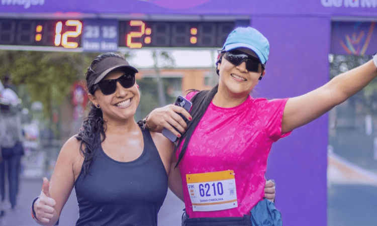 Dos participantes de la Carrera de la Mujer posan frente al arco de meta con números de competencia visibles
