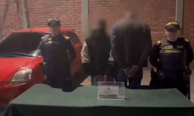 Dos personas capturadas de espaldas y esposados junto a dos policías 