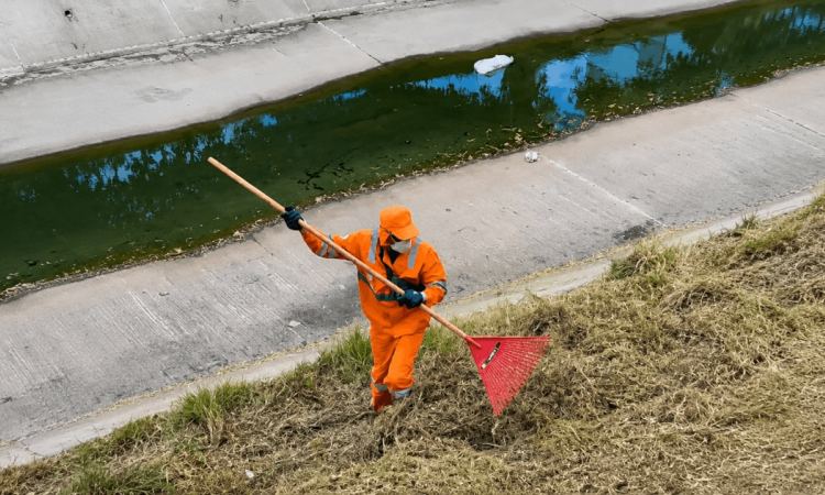 Foto que muestra una persona con el uniforme de Aguas Bogotá limpiando un canal de agua 