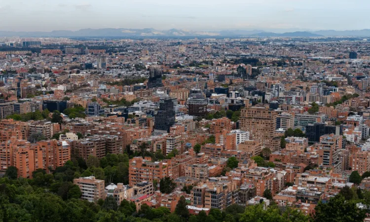 Vista panorámica de Bogotá con numerosos edificios residenciales y comerciales que se extienden por la ciudad, observados desde una zona elevada con vegetación en primer plano.