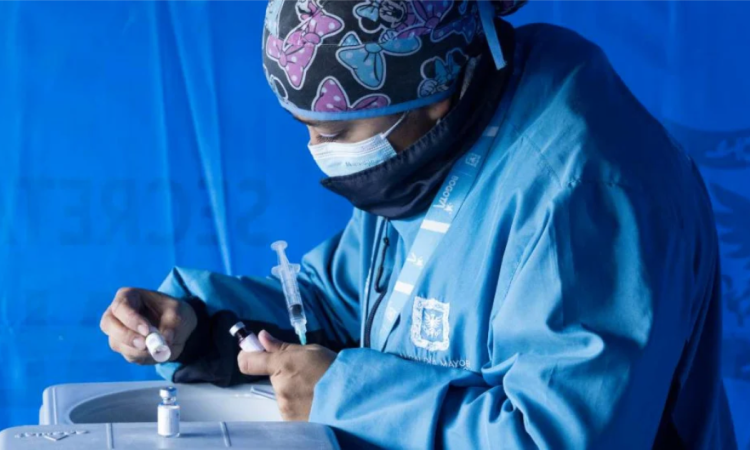Imagen de una mujer con traje de seguridad en salud preparando una vacuna.